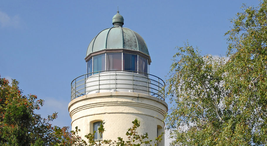 Hinter hohen Bäumen versteckt sich ein kleiner Leuchtturm